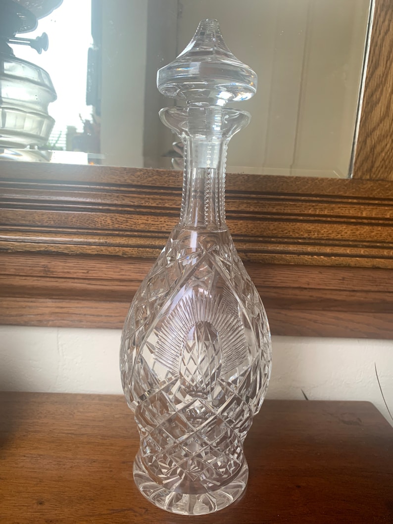 May include: A clear glass decanter with a cut crystal design and a stopper. The decanter has a tall, slender neck and a round body.