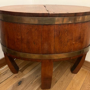 Peut inclure: Une table d'appoint en forme de tonneau en bois avec un dessus arrondi et articulé. La table est en bois brun foncé avec des bandes de laiton autour du haut et du milieu. Elle a trois pieds incurvés.