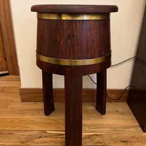 Peut inclure: Une table d'appoint en bois brun foncé avec un corps en forme de tonneau et trois pieds carrés. La table a des bandes de laiton autour du haut et du milieu. Le dessus est rond et plat.