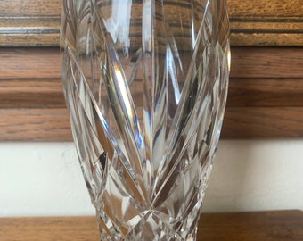 May include: A clear glass vase with a cut crystal design. The vase has a tall, cylindrical shape with a wide base.