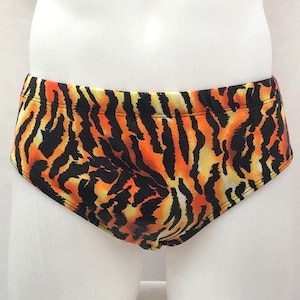 May include: Swim briefs featuring a tiger stripe design in orange, black, and yellow. The swimwear is displayed on a white mannequin. The briefs' bold pattern is a striking visual element.