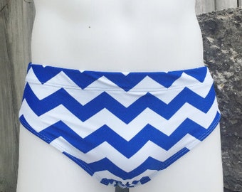 May include: White and blue chevron patterned swim briefs. The swimwear features a repeating zigzag design in bright blue against a white background. The briefs are displayed on a white mannequin.