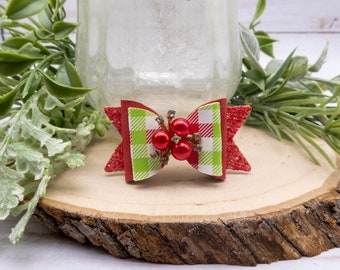 May include: A festive hair bow featuring a red glitter design with a green and white checkered center. The bow is adorned with red bead accents and silver rhinestones, perfect for holiday or special occasion wear.