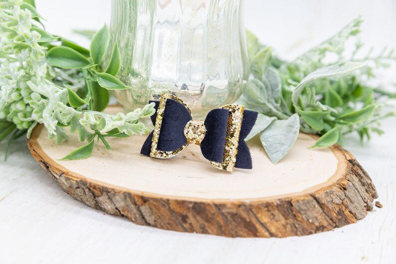 K&ouml;nnte beinhalten: Eine schwarze Samtschleife mit goldfarbenem Glitzerbesatz. Die Schleife liegt auf einer Holzscheibe.