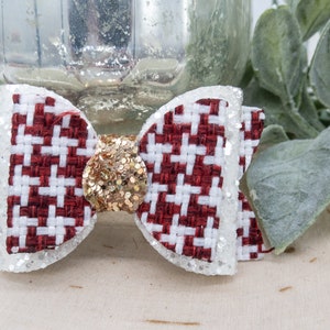 May include: A red and white checkered bow with gold glitter in the center. The bow is made of fabric and has a white border.