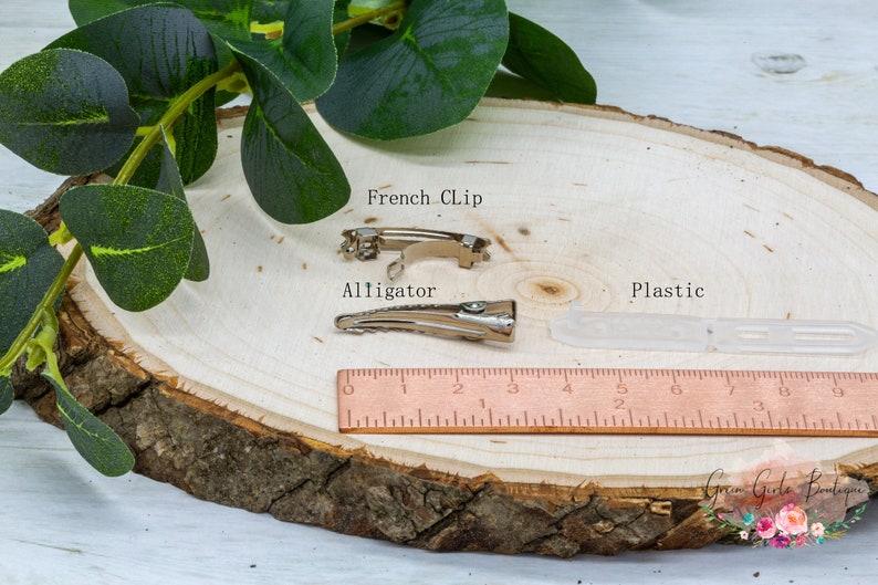 K&ouml;nnte beinhalten: Drei Arten von Haarklammern: eine silberne Alligator-Klammer, eine silberne franz&ouml;sische Klammer und eine transparente Plastikklammer. Die Klammern befinden sich auf einer Holzoberfl&auml;che mit einem Lineal als Gr&ouml;&szlig;enreferenz. Der Text "French Clip", "Alligator" und "Plastic" ist auf der Oberfl&auml;che geschrieben.