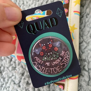May include: A dark blue QUAD button card with a round button that says "Meet Me Under The Mistle-Toe Stops". The button has a dark background with red and white accents. The card has a diamond design.