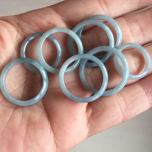May include: A collection of pale blue-green jade rings. The rings are round and appear to be made of a translucent material. The rings are held in a person's open hand.