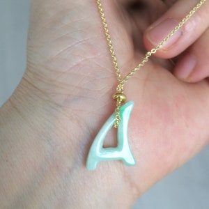 Op de afbeelding: Een gouden ketting met een lichtgroene jade hanger in de vorm van de letter 'A'.
