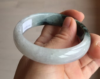 May include: A jade bangle bracelet with a white and green color scheme. The bangle is smooth and polished, with a subtle green hue throughout. The bangle is held in a hand, with the inside of the bangle facing the camera.