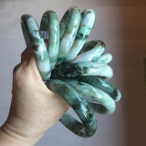 Peut inclure: Plusieurs bracelets en jade de différentes nuances de vert et de blanc. Les bracelets lisses et polis sont maintenus ensemble, mettant en valeur les veines et les motifs naturels de la pierre. Les bracelets sont un type de bijou populaire.