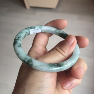 May include: A jade bangle bracelet in a light green and white colour. The bracelet has a label with the text "P240401 3025".