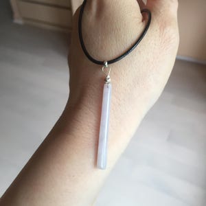 Op de afbeelding: Een eenvoudige ketting met een lange, dunne, lichtpaarse steen die aan een zwart koord hangt.