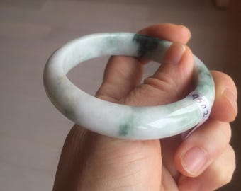 May include: A jade bangle bracelet with a light green color and white jade. The bangle has a smooth, polished finish and is a classic style.