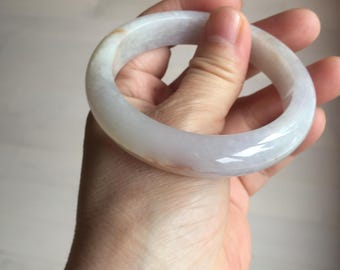May include: A translucent jade bangle bracelet. The bracelet is a pale green color with subtle variations and a smooth, polished surface. The circular shape is held in a hand, showcasing its elegant design.