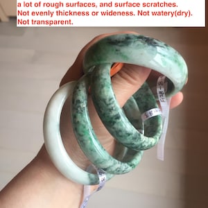 May include: Four jade bangles in shades of green, stacked on top of each other. The bangles are smooth and polished, with a slight variation in thickness. The bangles are labelled with numbers.