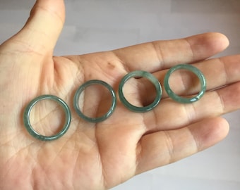 May include: Four jade rings in varying sizes, each with a translucent, pale green hue. The rings are smooth and circular, showcasing the natural variations in the stone. The rings are displayed on a hand.