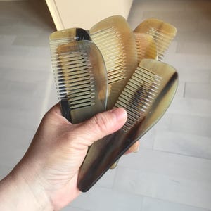 May include: A set of five brown and black combs made of horn. The combs are all different sizes and shapes, and they are arranged in a pile.