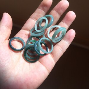 May include: A collection of jade rings in various shades of green, stacked and arranged in a hand.