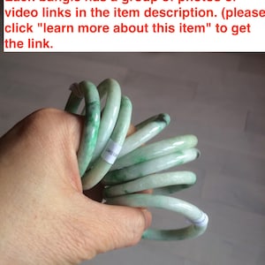 May include: Several jade bangles in shades of green and white are held together. The bangles display a smooth, polished finish, with each one exhibiting unique colour patterns. The image includes text.