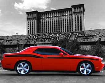 May include: A red Dodge Challenger with black racing stripes parked in front of a graffiti-covered building with the word "DETROIT" painted on it.