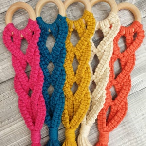 May include: Five macrame wall hangings with wooden rings. The hangings are in pink, teal, yellow, white, and orange.