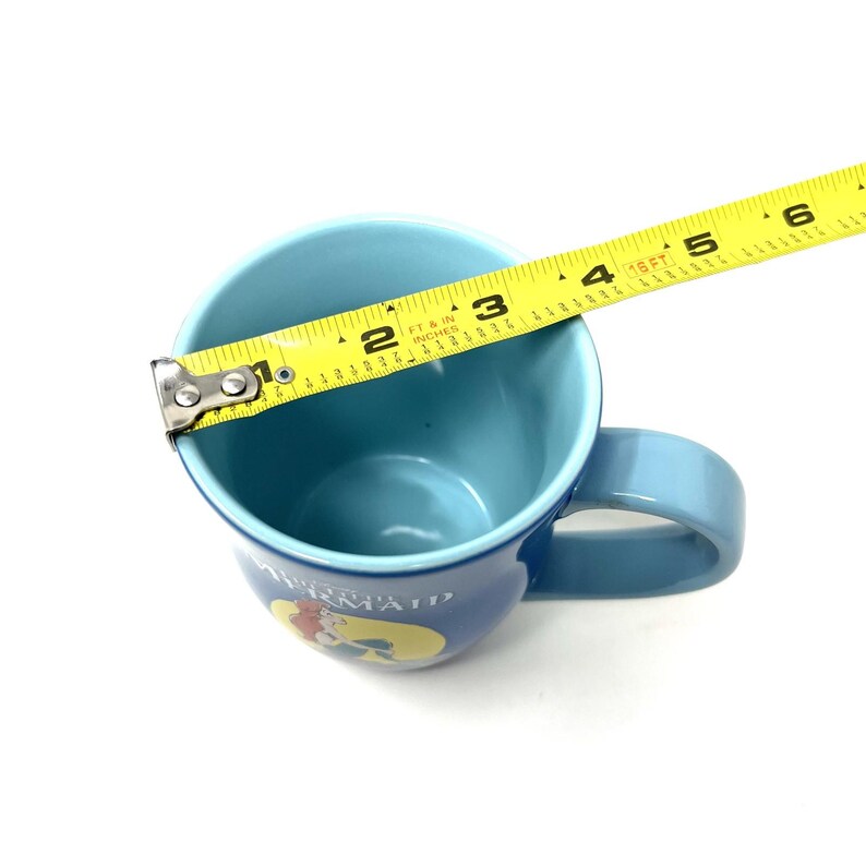 Pu&ograve; includere: Una tazza di ceramica blu con interno e manico azzurro. La tazza presenta una grafica di Ariel de La Sirenetta. La tazza ha un diametro di circa 7,6 cm.