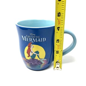 Pu&ograve; includere: Una tazza di ceramica blu con il film Disney "La Sirenetta". La tazza ha un manico e un interno azzurro chiaro. Il design include Ariel, la sirena, e il titolo del film. La tazza &egrave; alta circa 10 cm.