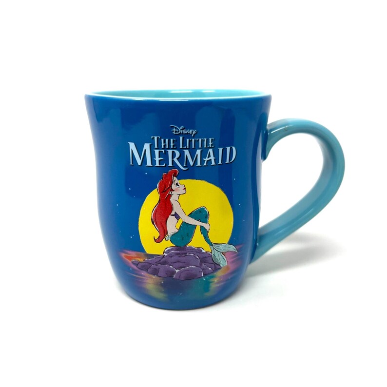 Pu&ograve; includere: Tazza in ceramica blu con il film Disney "La Sirenetta". La tazza ha un interno e un manico azzurri. Il disegno mostra Ariel con i capelli rossi e la coda turchese, seduta su una roccia davanti a una luna gialla.