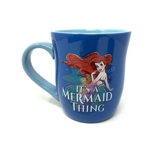 Pu&ograve; includere: Tazza in ceramica blu con Ariel de La Sirenetta. La tazza ha un manico e un interno azzurro. La parte anteriore della tazza mostra Ariel con la scritta "It's a Mermaid Thing."