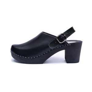 May include: Black leather heeled clog with a buckle strap and a white stitch detail around the sole.