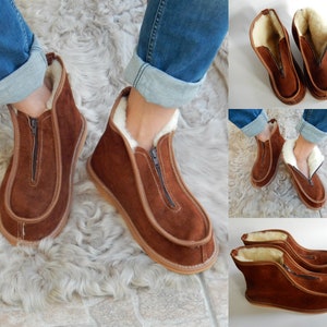 May include: Brown leather slippers with a zipper and a white sheepskin lining. The slippers are shown on a fluffy white rug.
