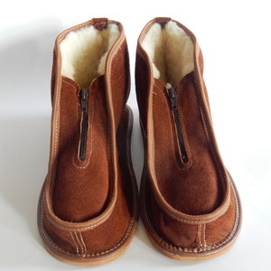 May include: A pair of brown suede slippers with a zipper up the front and a white sheepskin lining.