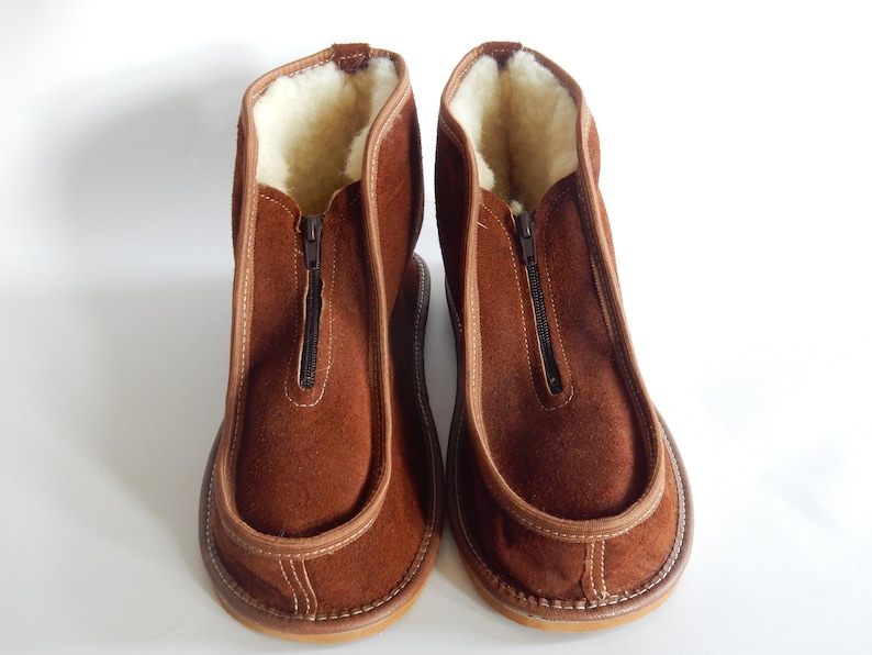May include: A pair of brown suede slippers with a zipper up the front and a white sheepskin lining.