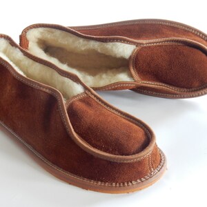 May include: A pair of brown suede slippers with a sheepskin lining. The slippers have a simple design and are perfect for keeping your feet warm in the winter.