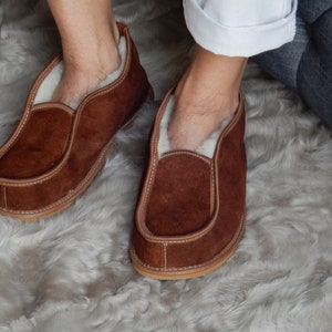 May include: A pair of brown suede slippers with a white sheepskin lining. The slippers are worn and have a slightly distressed look.