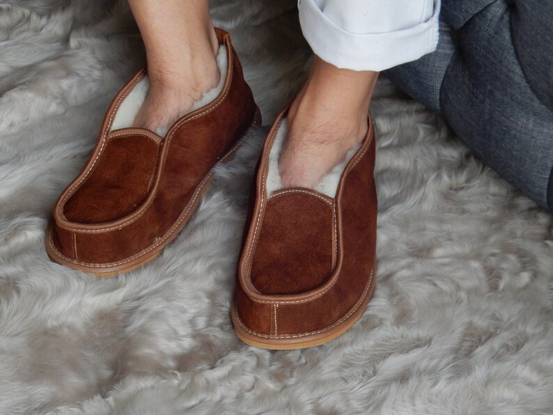 May include: A pair of brown suede slippers with a white sheepskin lining. The slippers are worn and have a slightly distressed look.