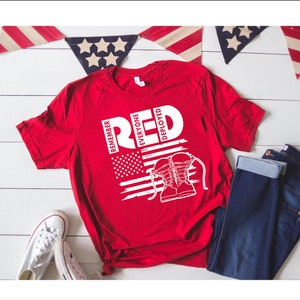 Könnte beinhalten: Rotes T-Shirt mit weißem Grafikdesign. Das Design zeigt das Wort "RED", die amerikanische Flagge und Kampfstiefel. Der Text "Remember Everyone Deployed" ist ebenfalls enthalten. Ein lässiges Kleidungsstück.