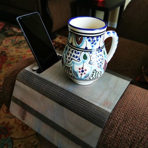 Könnte beinhalten: Ein Holzarmlehnentablett mit einem schwarz-weißen Streifenmuster. Ein Smartphone befindet sich im Telefonhalter und eine Tasse mit blau-weißem Muster steht auf dem Tablett.