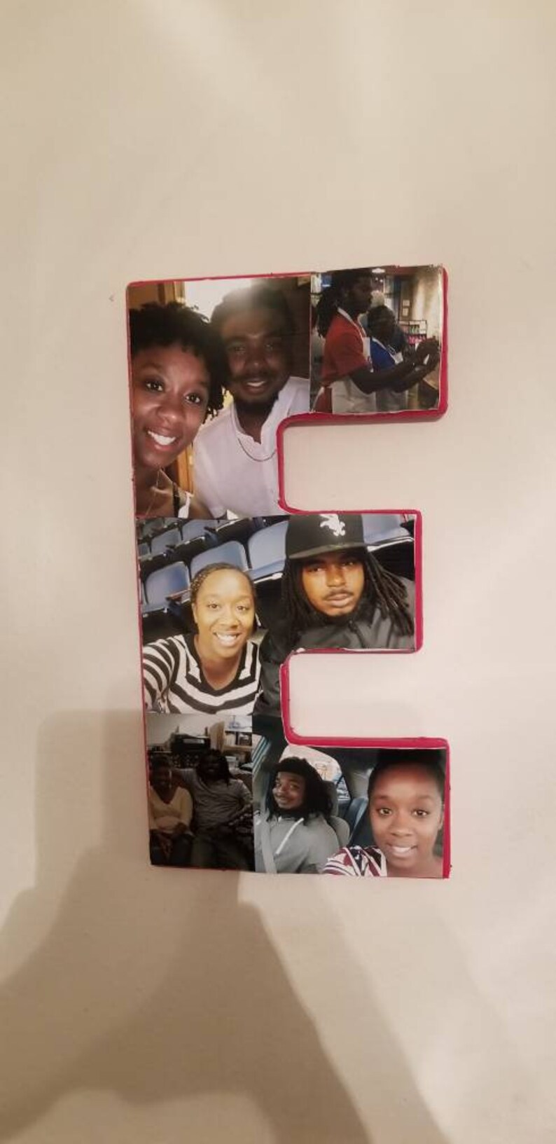 Pu&ograve; includere: Una lettera "E" in legno con bordo rosso, riempita con pi&ugrave; fotografie di persone. Le foto mostrano varie persone che sorridono e posano, creando un collage fotografico personalizzato.
