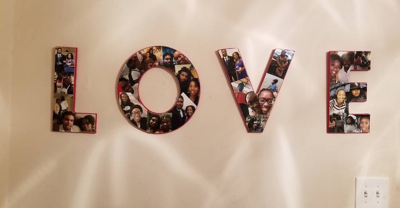 Pu&ograve; includere: La parola "LOVE" esposta su un muro, ogni lettera costruita da singole fotografie. Le lettere hanno un bordo rosso e le foto presentano varie persone. Le lettere sono montate su un muro di colore chiaro.