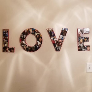 Pu&ograve; includere: La parola "LOVE" esposta su un muro, ogni lettera costruita da un collage di fotografie. Le lettere hanno un bordo rosso e le foto presentano varie persone. Il muro &egrave; di colore beige chiaro.