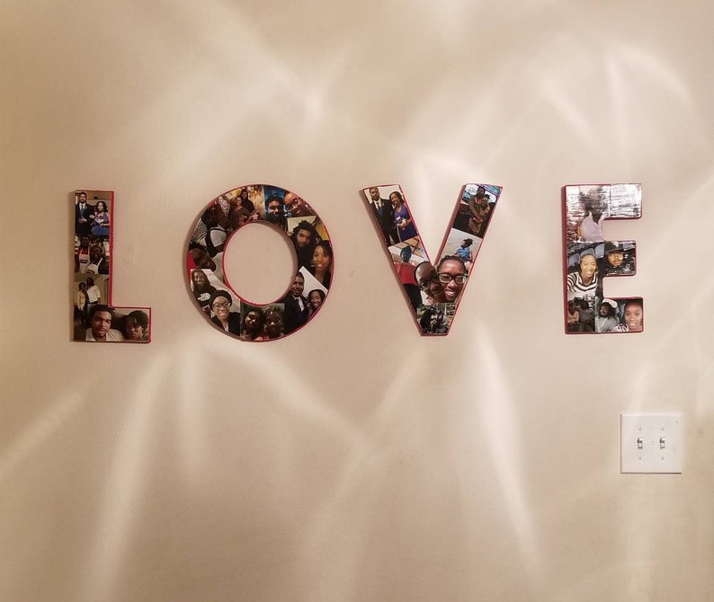 Pu&ograve; includere: La parola "LOVE" esposta su un muro, ogni lettera costruita da un collage di fotografie. Le lettere hanno un bordo rosso e le foto presentano varie persone. Il muro &egrave; di colore beige chiaro.