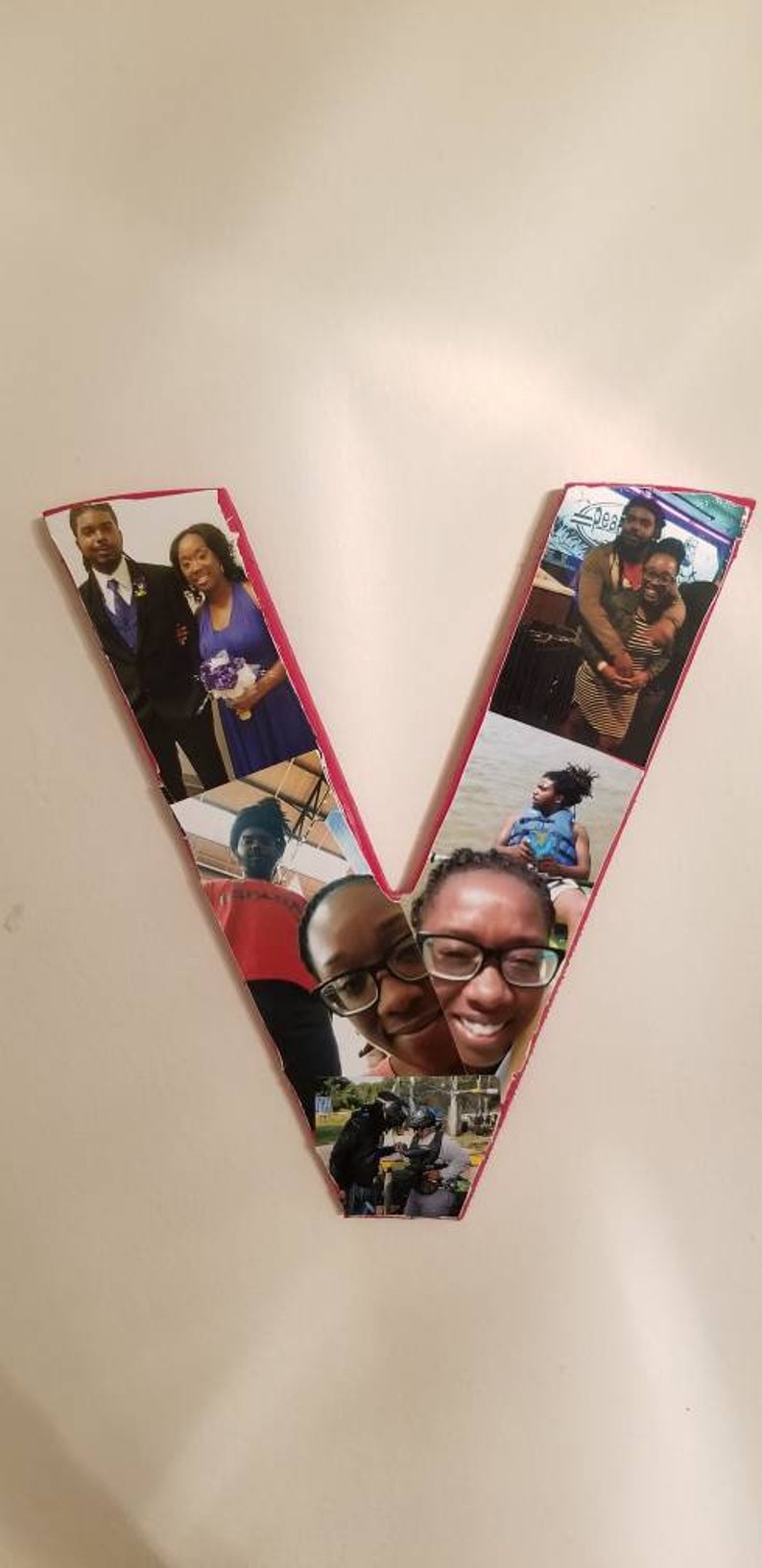 Pu&ograve; includere: Una lettera "V" in legno decorata con pi&ugrave; fotografie. Le foto raffigurano persone in vari contesti, tra cui un matrimonio, abbracci e un giro in moto d'acqua. I bordi della lettera sono delineati in rosa.