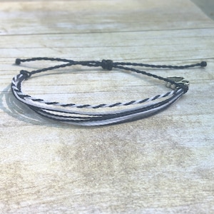 May include: A black and white braided bracelet with a silver heart charm.