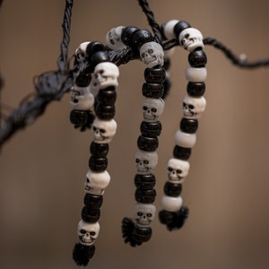 Op de afbeelding: Drie zwart-witte schedel kralen armbanden hangen aan een tak. De armbanden zijn gemaakt van afwisselende zwarte en witte kralen met schedel ontwerpen.