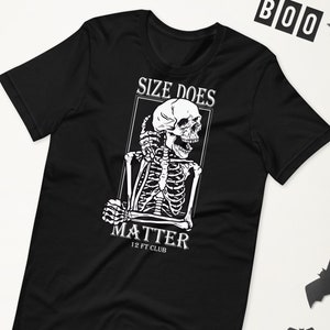 Op de afbeelding: Zwart T-shirt met een witte afbeelding van een skelet met de tekst "Size Does Matter 12 Ft Club".