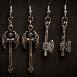 May include: Four silver axe earrings with a detailed design. The earrings are on a black background.