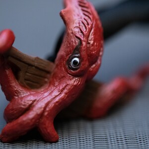 May include: A red plastic octopus toy with a single eye, holding a small wooden boat in its tentacles.