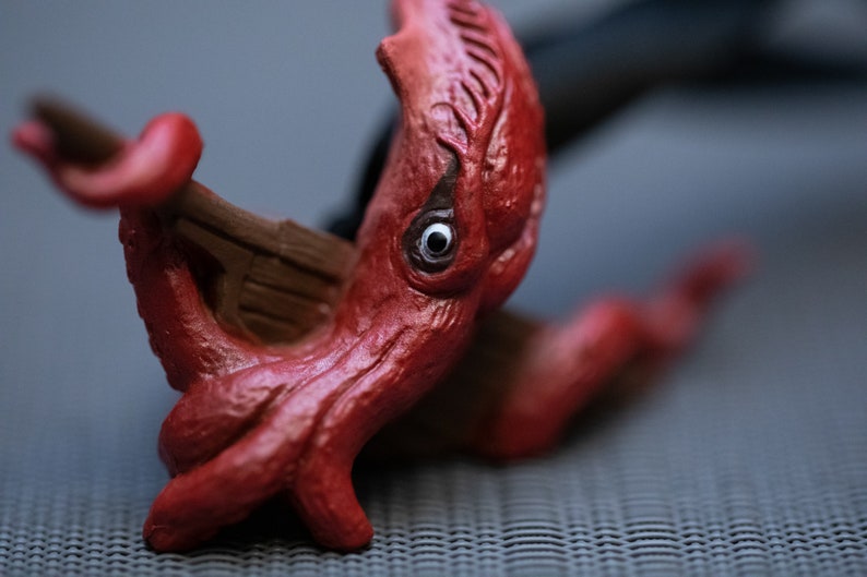 May include: A red plastic octopus toy with a single eye, holding a small wooden boat in its tentacles.